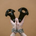 Hands wrapped in chains holding virtual reality controllers, symbolizing how technology is changing ownership into ongoing corporate control.