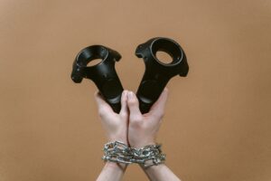 Hands wrapped in chains holding virtual reality controllers, symbolizing how technology is changing ownership into ongoing corporate control.