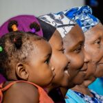 Four generations of a family shown in profile, from a young child to a great-grandmother, wearing colorful traditional headwraps
