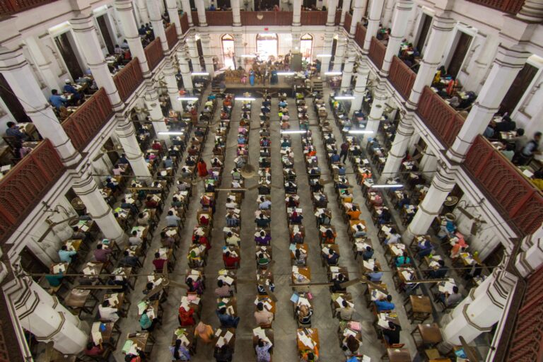 Overhead view of hundreds of students taking a competitive exam in a colonnaded heritage hall in India