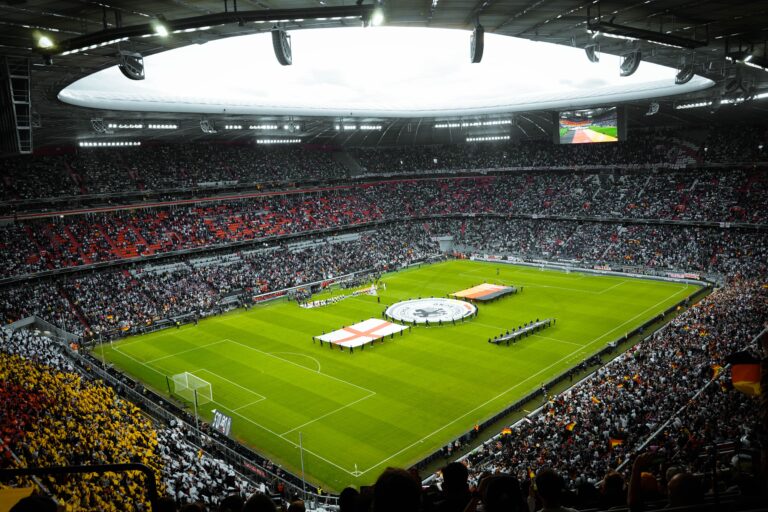 A packed football stadium before kickoff, with tens of thousands of supporters gathered around the pitch during a major international match.