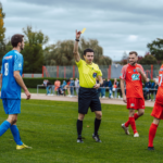 Football referee issuing a yellow card during a match as players react.