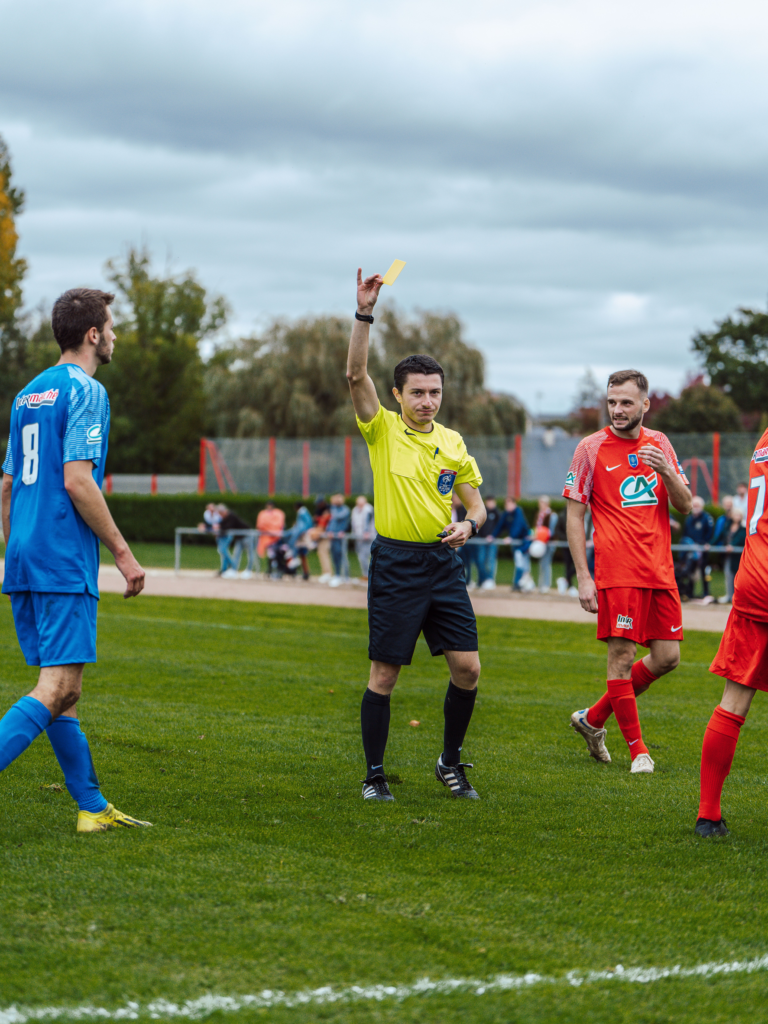 Football referee issuing a yellow card during a match as players react.