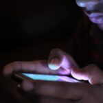 Person using a glowing smartphone in the dark, representing the rise of betting, trading and speculation apps