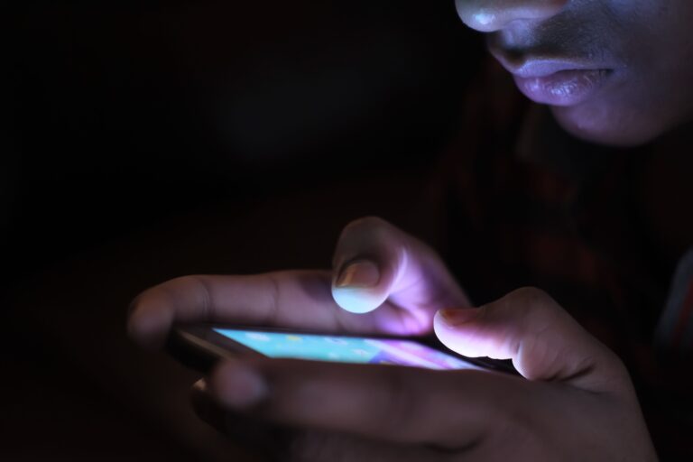 Person using a glowing smartphone in the dark, representing the rise of betting, trading and speculation apps