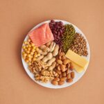 Plate showing salmon, beans, lentils, chickpeas, nuts and cheese as protein-rich foods