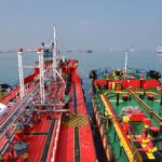 Two oil tankers positioned side by side at sea, with deck pipelines visible during a ship-to-ship transfer operation.